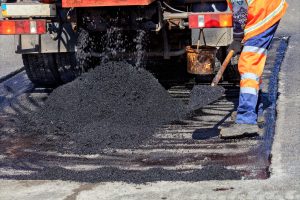 A Road Service Worker Shoveling New Asphalt During Construction And Patching Of A Road - Big Easy Asphalt